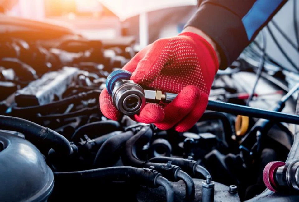 Technician holding A/C refrigerant fill line above engine bay